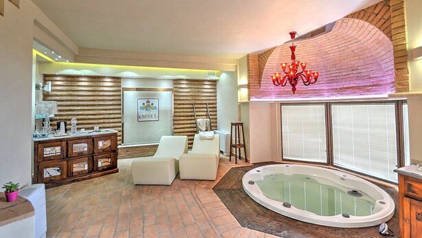 Um espaço tipo spa com banheira de hidromassagem, poltronas de descanso brancas, um armário de madeira e uma parede de tijolos.