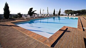 Piscina retangular com superfície de água azul cristalina, rodeada por um deck de madeira e cadeiras de lounge brancas.