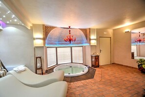 A spa room with a hot tub, a massage table, and a large arched window.