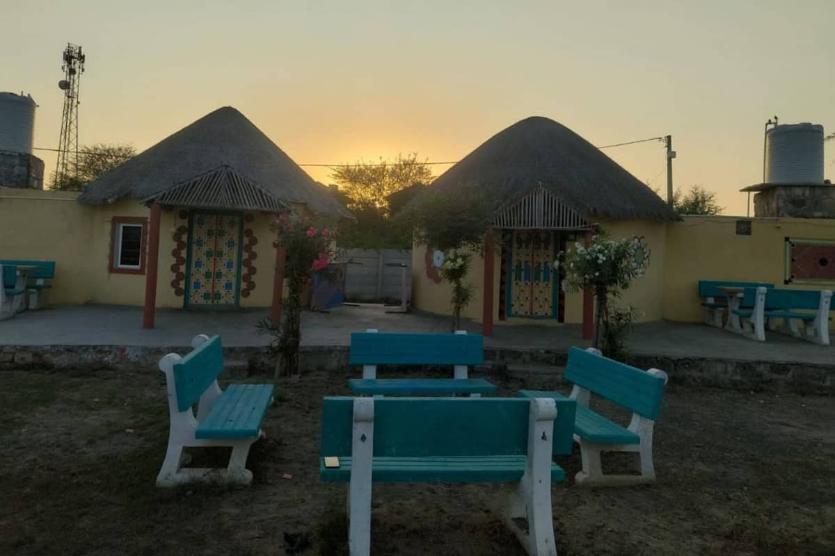 A courtyard with two thatched-roof structures, benches, and water tanks.