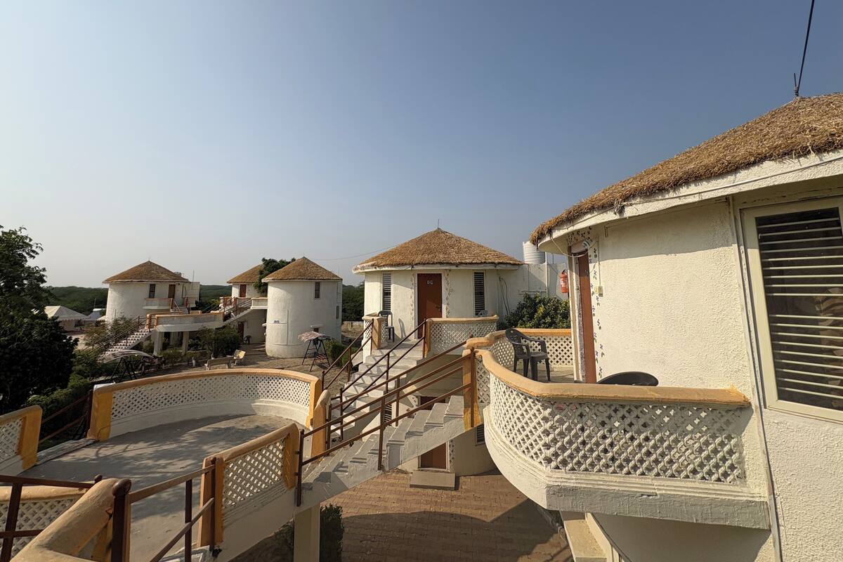 A residential area with multiple houses featuring thatched roofs and white walls, connected by a bridge with a wooden railing.