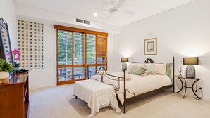A bedroom with a large window, a bed with a headboard, bedside lamps, and a small table with a lamp.