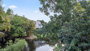 Un entorno tranquilo junto al río, con abundante vegetación y un edificio moderno al fondo.