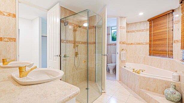 A modern bathroom with a glass-enclosed shower, a freestanding bathtub, and a vanity with gold fixtures.