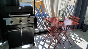 A balcony with a grill, a table, and chairs. - LOVELY ALL-INCLUSIVE GROUND-FLOOR 2-BEDROOM APARTMENT WITH TWO TVS AND WIFI NETFLIX (Le Barcarès)