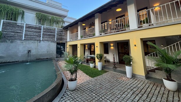A courtyard with a pool, potted plants, and a two-story building with balconies. - Baron's antiquarian villa (Kochi)