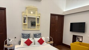 A hotel room with a large bed, a television, a mirror, and a yellow armchair. - Baron's antiquarian villa (Kochi)