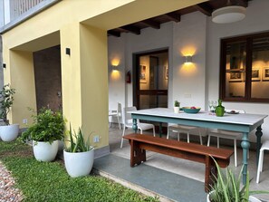 Un espace extérieur aménagé avec un banc en bois, une table blanche et des plantes en pot.