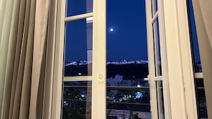 Ein Fenster mit Blick auf nächtliche Stadtansicht, darunter eine beleuchtete Brücke und Gebäude.