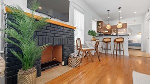 A modern living room with a fireplace, wooden flooring, and a dining area with bar stools.
