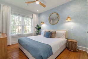 A bedroom with a bed, a ceiling fan, a window with curtains, a plant, and a wall-mounted mirror. - Casita Azul l Walk to DT l Mins to Beach (St. Augustine)