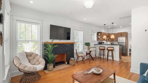 A modern living room with a fireplace, a dining area, and a kitchen with bar stools.