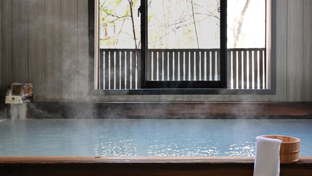 A traditional Japanese onsen with a wooden bench and a wooden bucket. - Komakusa Hotel (Matsumoto)