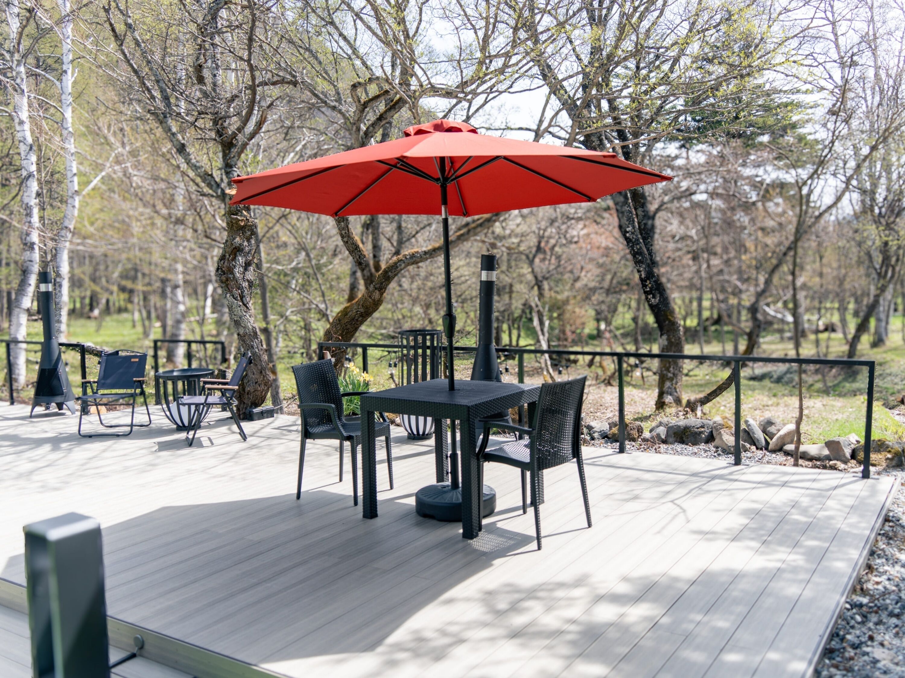 Un patio al aire libre con una mesa, sillas, un paraguas rojo y una parrilla negra.