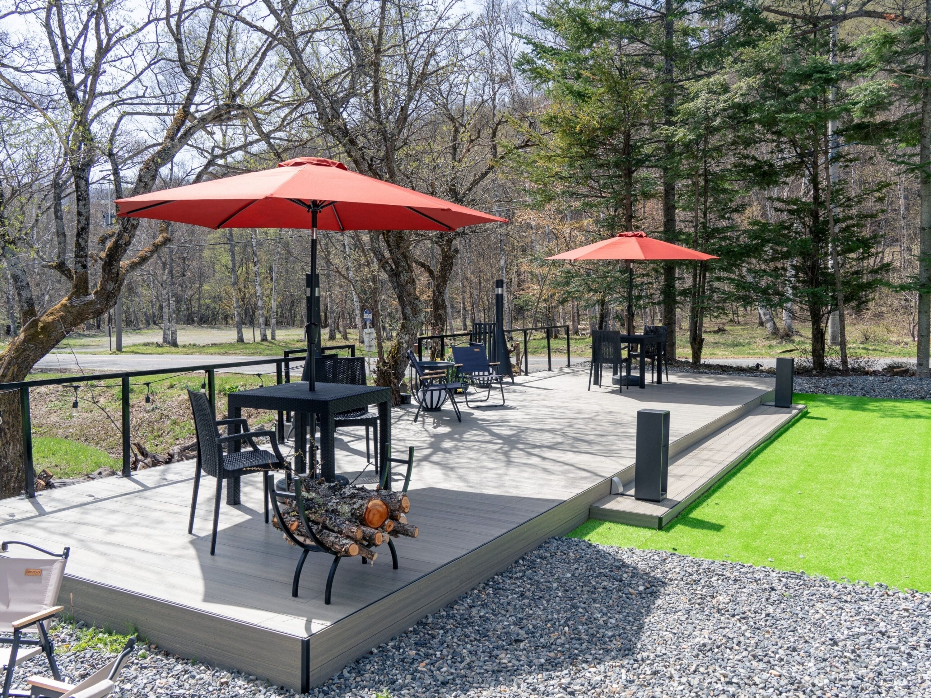Un espace extérieur aménagé en terrasse, avec des tables et des chaises, des parasols rouges et une plateforme en bois.