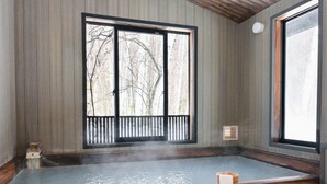 A traditional Japanese onsen with a wooden deck, a wooden bench, and a view of bare trees through the sliding doors. - Komakusa Hotel (Matsumoto)