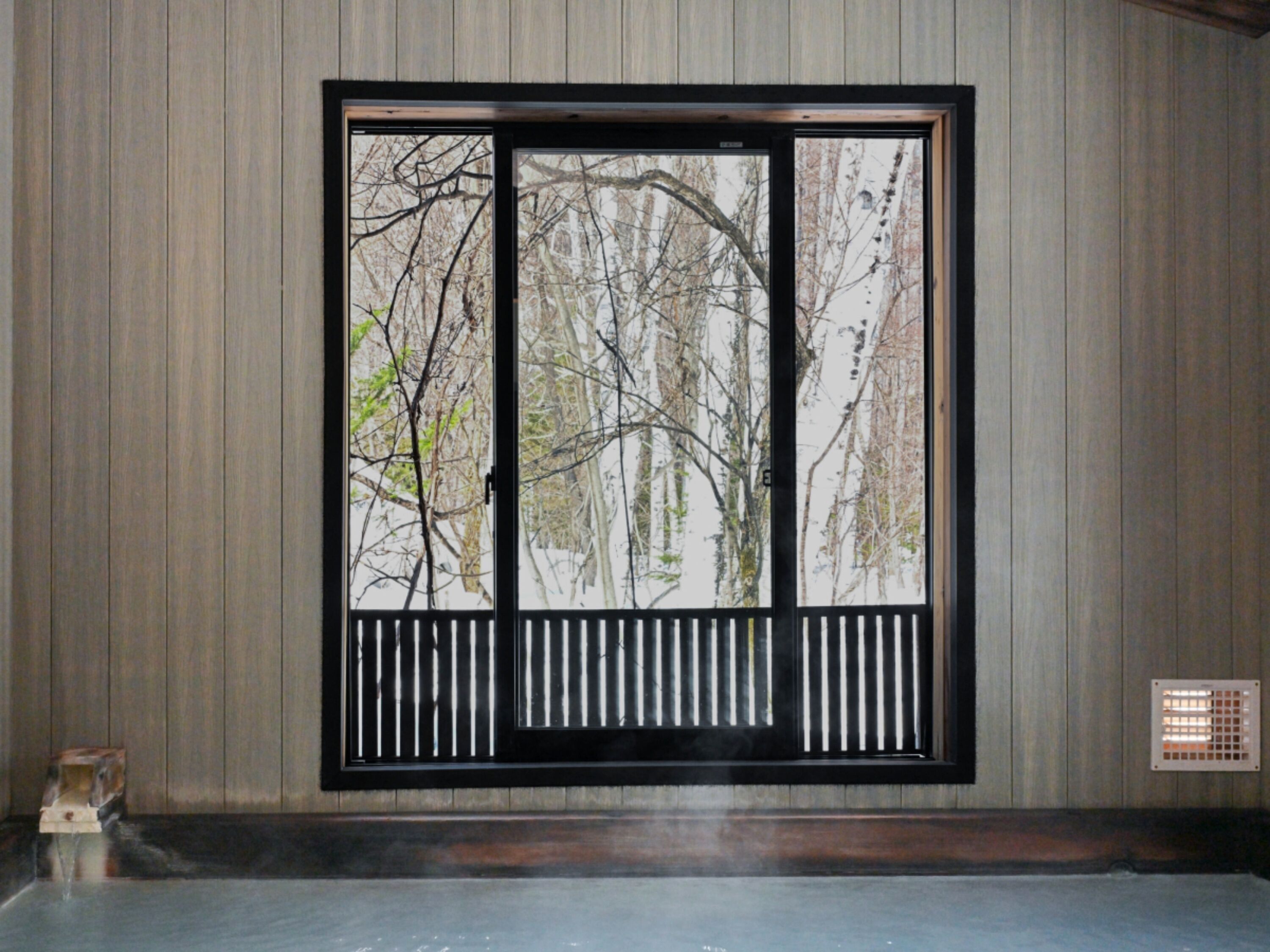 A room with a large window featuring a black frame and a white railing.