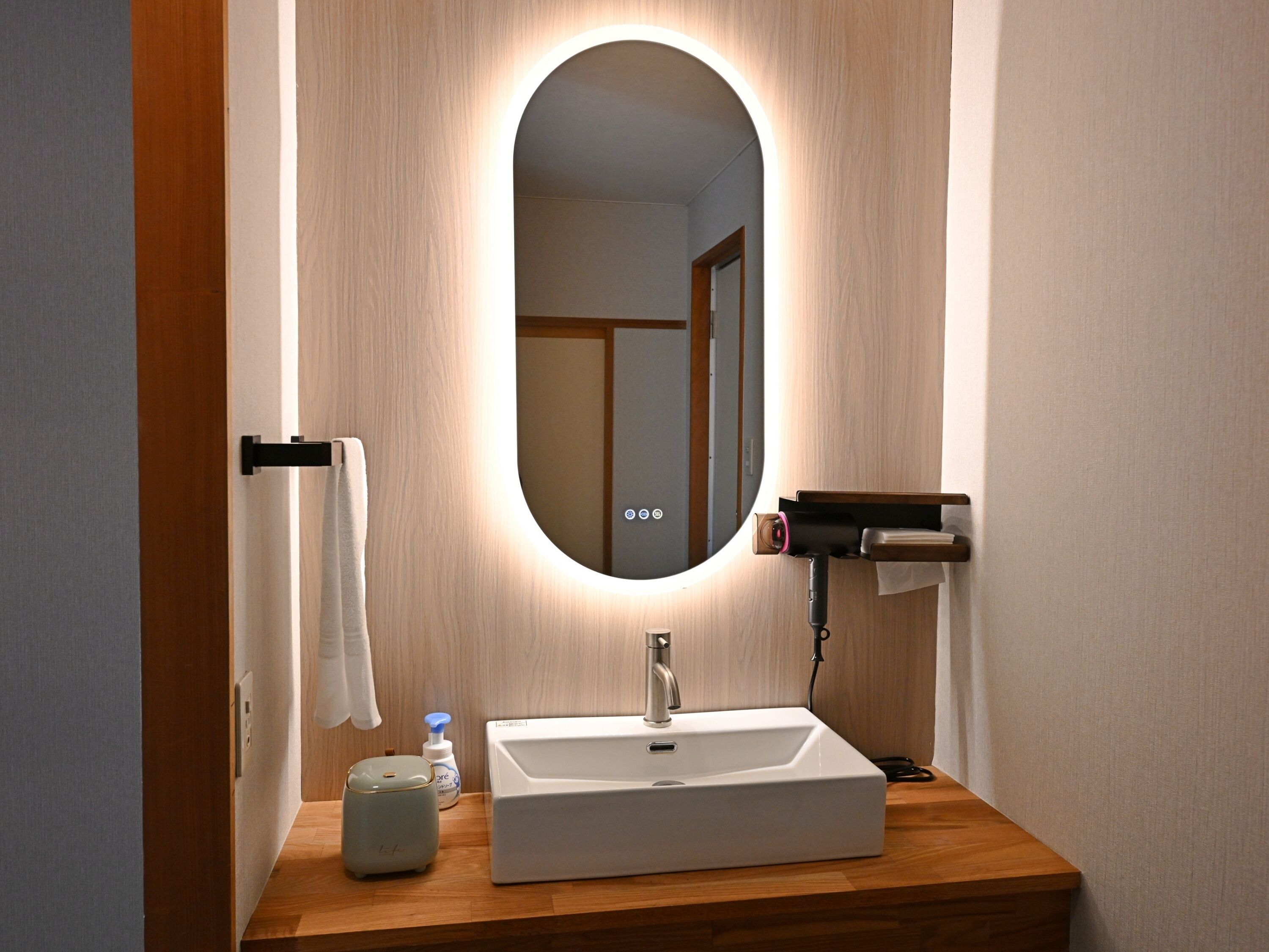 A bathroom with a white sink, a mirror, a towel rack, a soap dispenser, and a hairdryer.