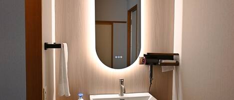A bathroom with a white sink, a mirror, a towel rack, a soap dispenser, and a hairdryer.