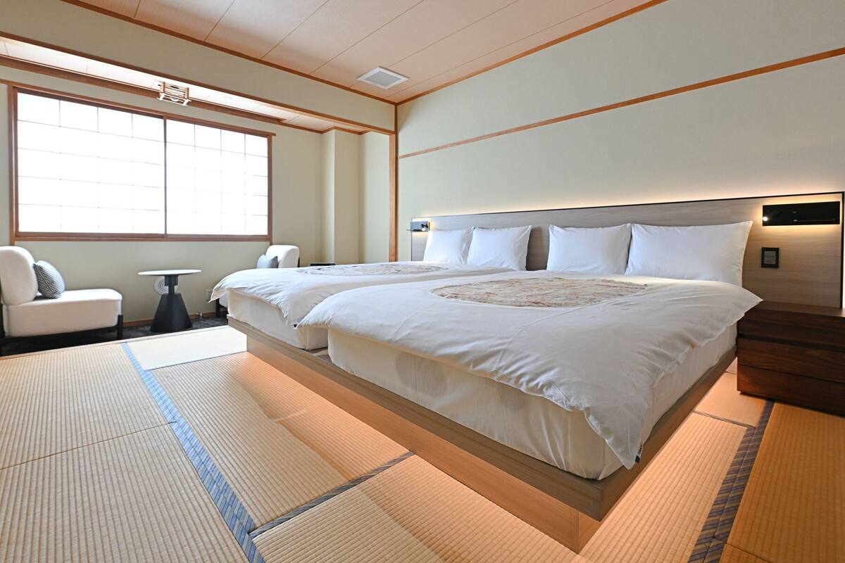 Habitación de hotel con una cama grande, una mesita, una silla y un ventanal amplio.