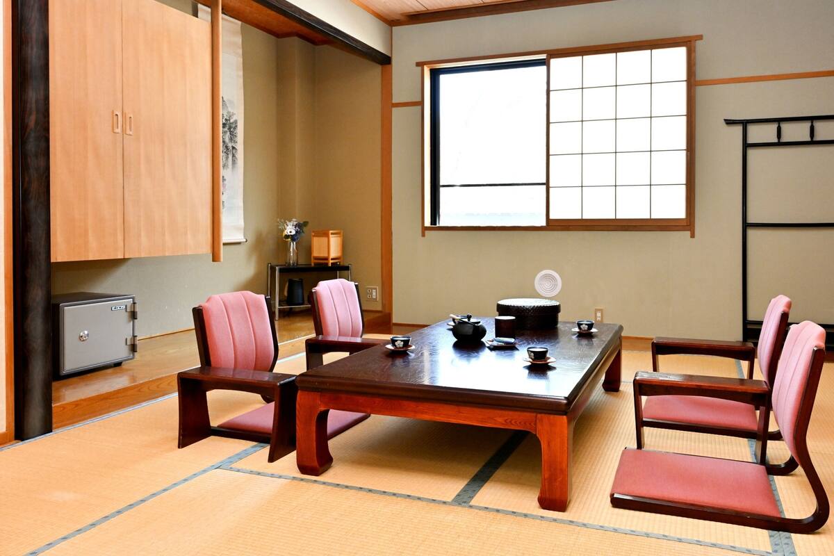Una habitación japonesa tradicional con suelo de tatami, una mesa de madera baja y sillas con cojines rojos.