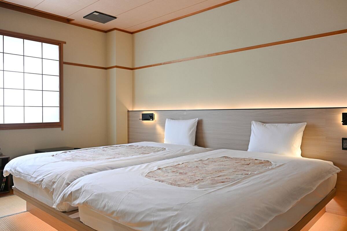 Una habitación de hotel con dos camas, un ventanal grande y un cabecero de madera.