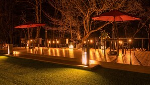 An outdoor patio area with wooden flooring, red umbrellas, and seating arrangements. - Komakusa Hotel (Matsumoto)