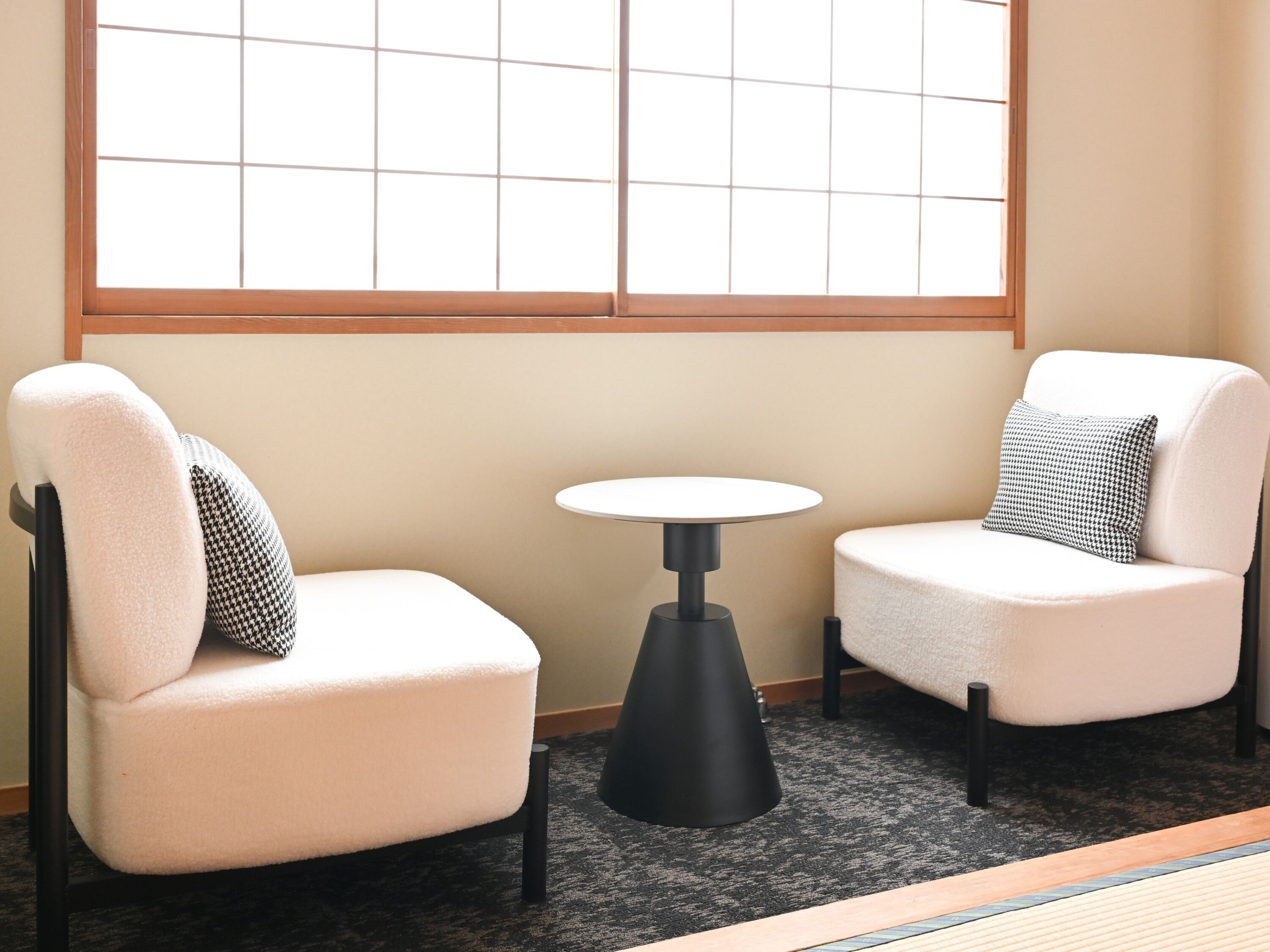 Two white armchairs with black and white patterned cushions, a small black table, and a window with a grid pattern.