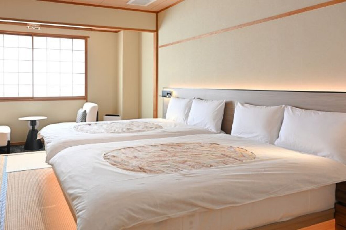 Een hotelkamer met twee bedden, een groot raam en een traditionele Japanse tatami mat.