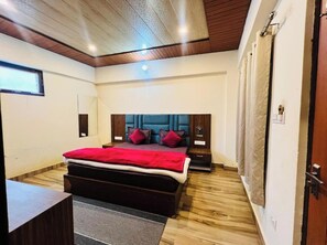 A bedroom with a bed, wooden flooring, a headboard, nightstands, a desk, and a window. - Hotel Maa Bhuvneswari (Badrinath)