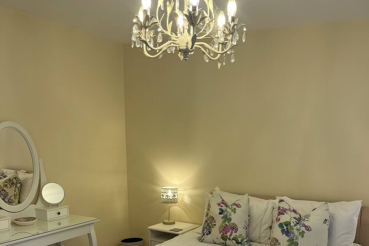 Un dormitorio ordenado con cama, una mesita de noche con lámpara, cómoda con espejo y candelabro.