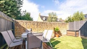 A patio with a table and chairs, a stone wall, and a wooden deck.