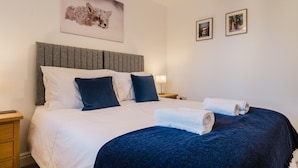 A hotel room with a large bed, a grey headboard, white and dark blue pillows, and two framed pictures on the wall.