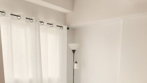 A bedroom with a bed, curtains, a nightstand, a lamp, and a rug. - Meteor Garden (Cebu City)