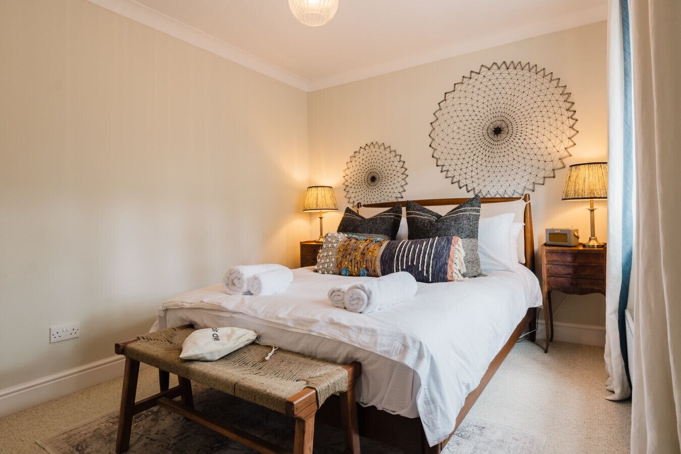 A neatly arranged bedroom with a bed, bedside lamps, a bench, and decorative wall art.