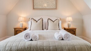 Una cama bien hecha con dos almohadas, dos lámparas de noche y toallas enrolladas sobre el cabecero.
