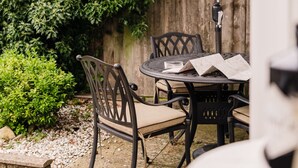Un patio al aire libre con una mesa, dos sillas, un paraguas grande y una valla de madera cubierta de follaje.