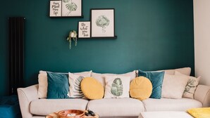 A living room with a teal wall, a beige sofa with patterned cushions, a wooden coffee table, and framed artwork. - Beautiful 3 Bedroom Home Near Worcester (Kempsey)