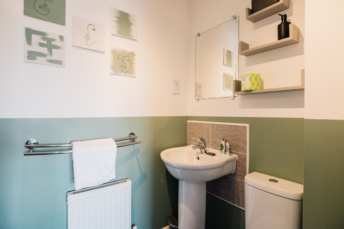 A bathroom with a towel rack, sink, and toilet. There are wall-mounted shelves with toiletries.