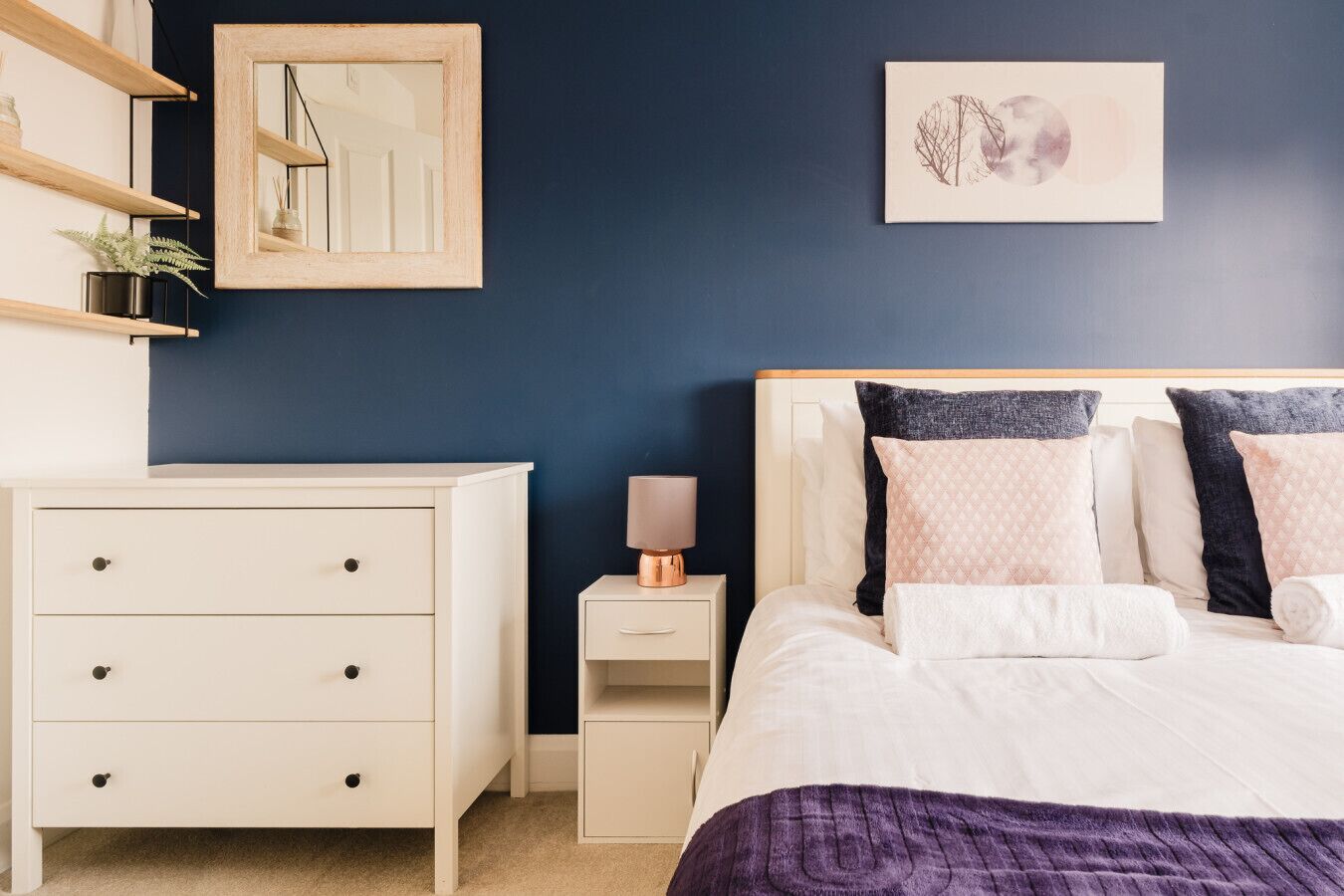 Ein Schlafzimmer mit Bett, Nachttisch, Kommode und Spiegel an der Wand.