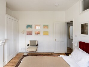 Un dormitorio con cama, una silla, un tapete y obras de arte en la pared.