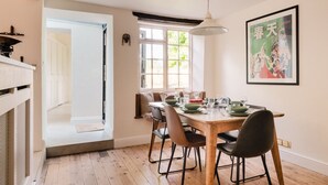 Un comedor con una mesa de madera dispuesta para cuatro personas, rodeada de sillas. Un ventanal grande proporciona luz natural y se observa una obra de arte enmarcada en la pared.