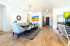 A modern dining area with a wooden table and chairs, a patterned rug, and a clock on the wall. - Relax in Style at Paradise Village – Pool & Pickleball! (Santa Clara)