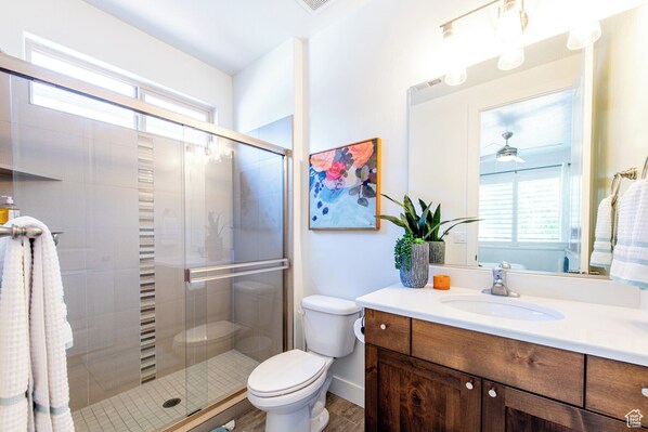 A modern bathroom with a glass-enclosed shower, a toilet, a sink with a wooden vanity, and a large mirror. - Paradise Village Retreat - Lazy River, Pools & Pickleball (Santa Clara)