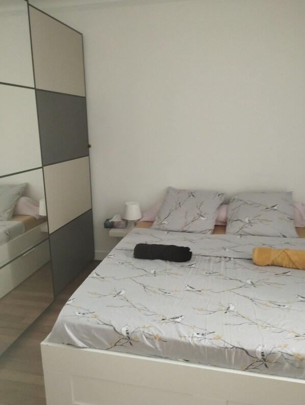 A bedroom with a bed, pillows, a bedside table, and a mirror.