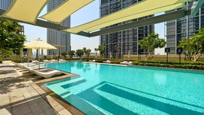 A swimming pool with lounge chairs and umbrellas, surrounded by high-rise buildings. - Creek Rise Residences - Creek Harbour (Dubai)