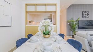 A modern dining area with a white table set for four, blue chairs, and a vase of white orchids. - Creek Rise Residences - Creek Harbour (Dubai)