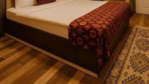 A hotel room with a large bed, a headboard, a mirror, and a patterned rug. - Bella Garden Hotel (Baku)
