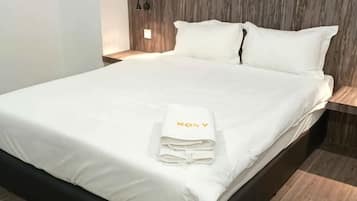 A neatly made bed with a folded white towel and a pillow with 'ROYAL' embroidered on it.