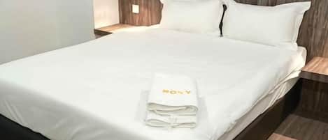 A neatly made bed with a folded white towel and a pillow with 'ROYAL' embroidered on it.
